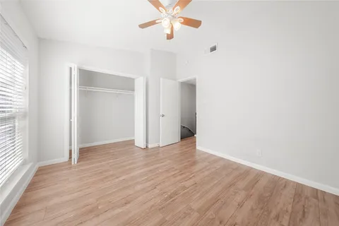 an empty room with wooden floor chandelier fan and windows