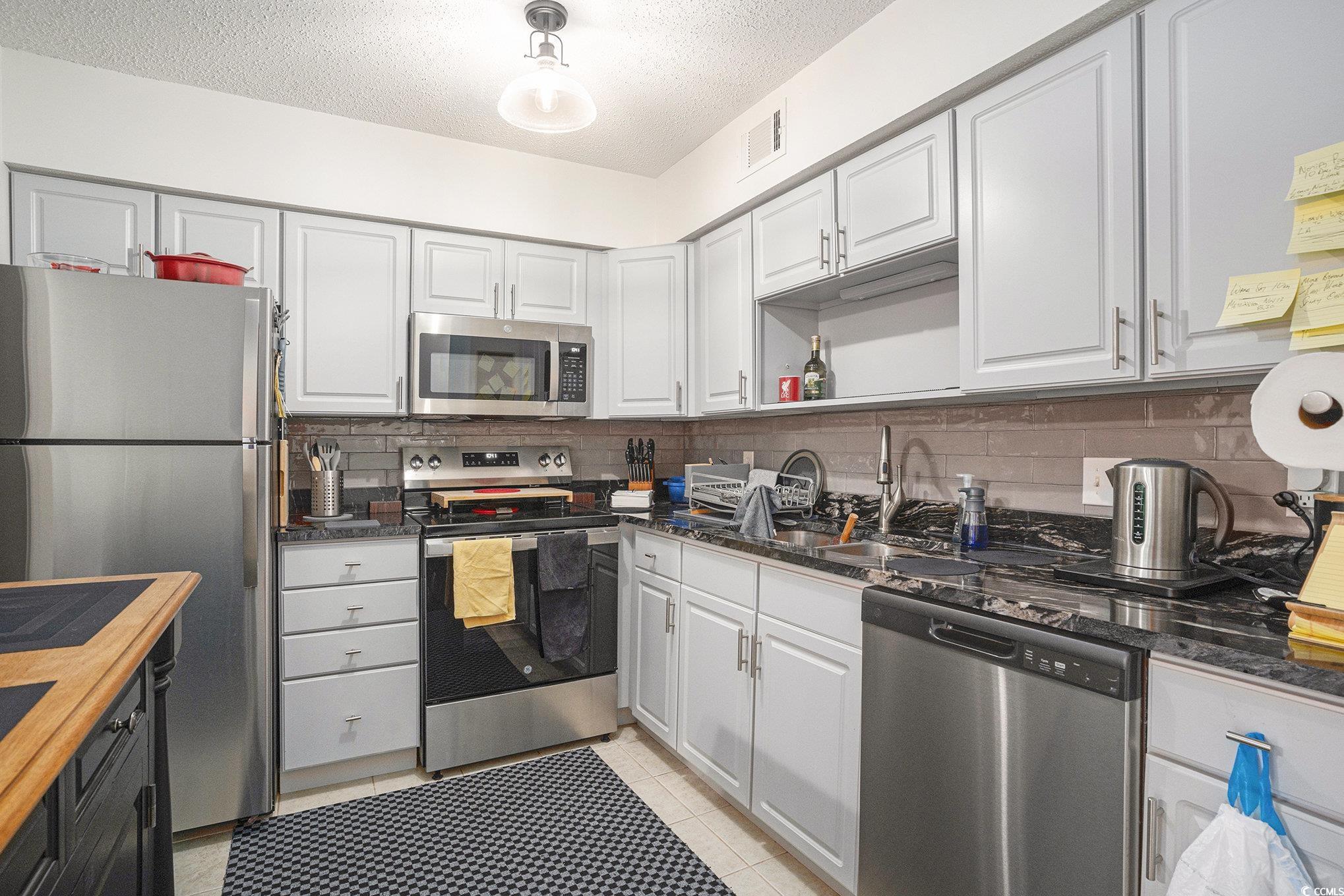 400 Cambridge Circle, Unit L8 Murrells Inlet, SC 29576 - Photo 5 of 22 Kitchen with appliances with stainless steel finishes, a textured ceiling, white cabinetry, and light tile patterned floors