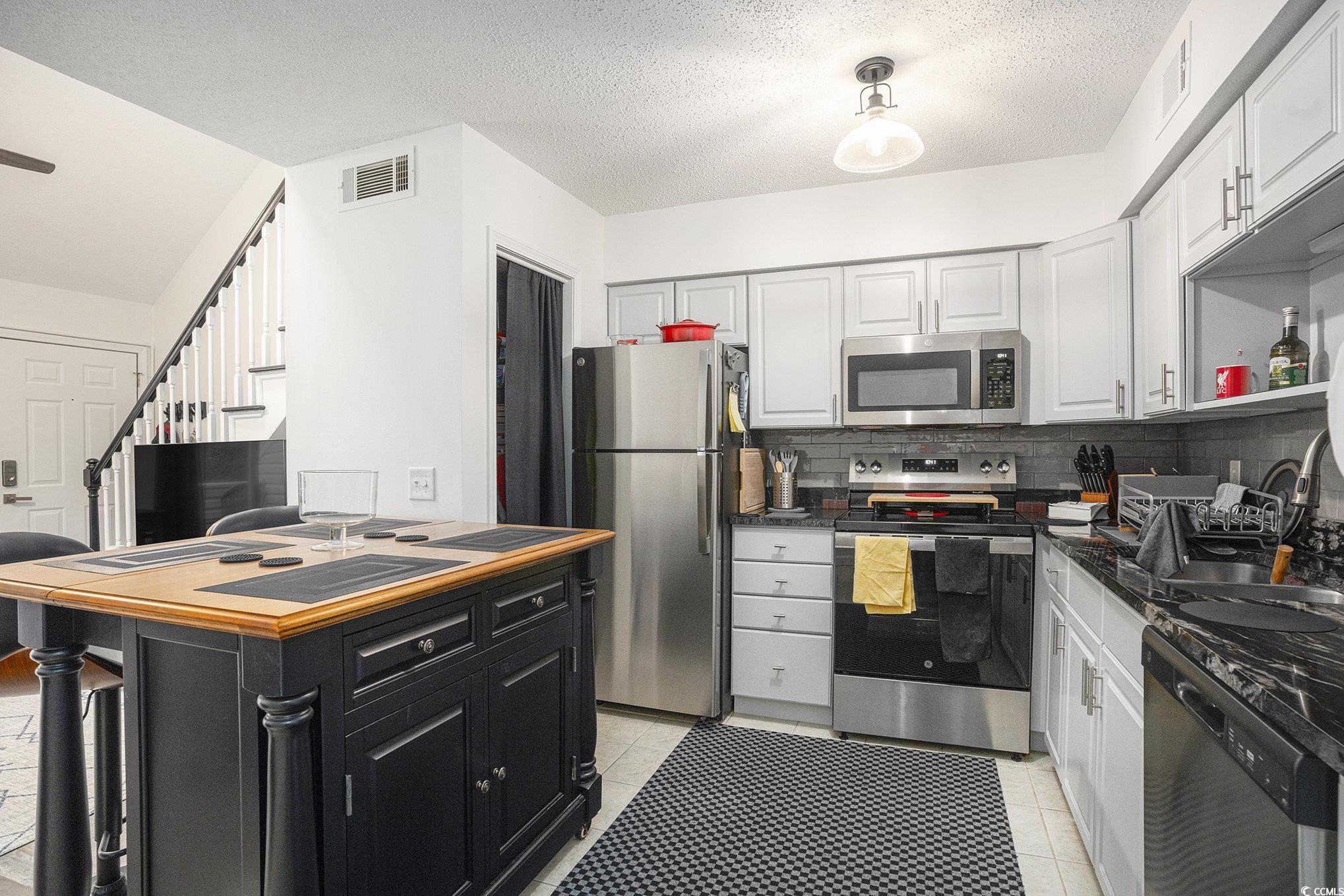 400 Cambridge Circle, Unit L8 Murrells Inlet, SC 29576 - Photo 6 of 22 Kitchen with stainless steel appliances, a textured ceiling, light tile patterned floors, decorative backsplash, and dark cabinetry