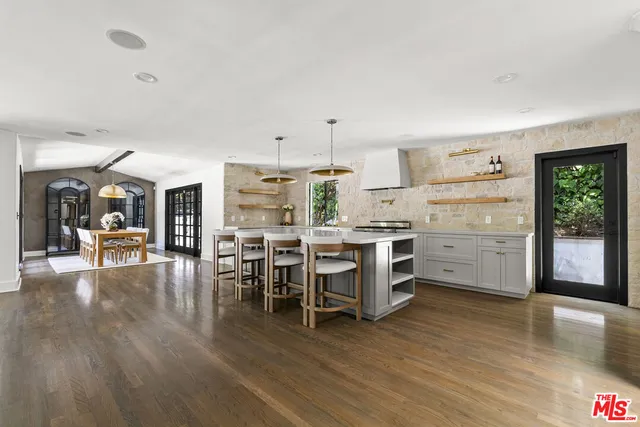 a kitchen with stainless steel appliances a stove a sink a oven a dining table and chairs with wooden floor