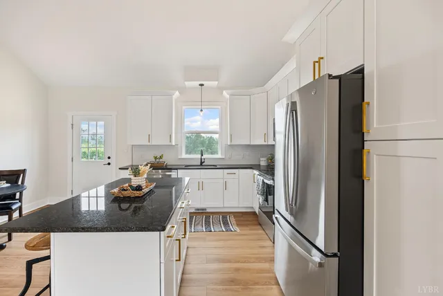 a kitchen with granite countertop a refrigerator a sink a stove and white cabinets