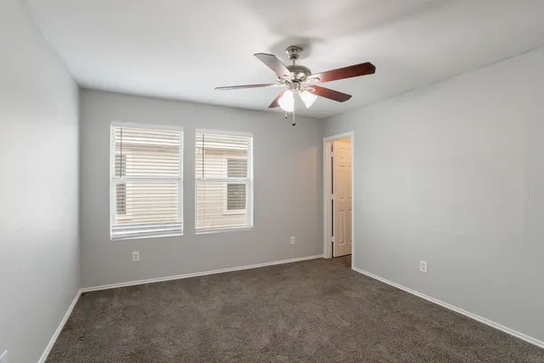 an empty room with a chandelier fan and windows