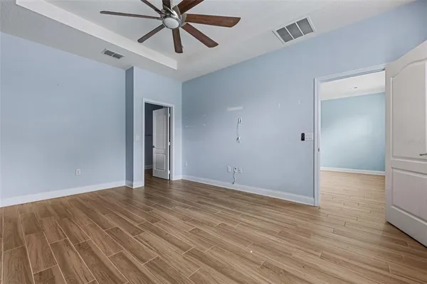 an empty room with wooden floor chandelier fan and windows