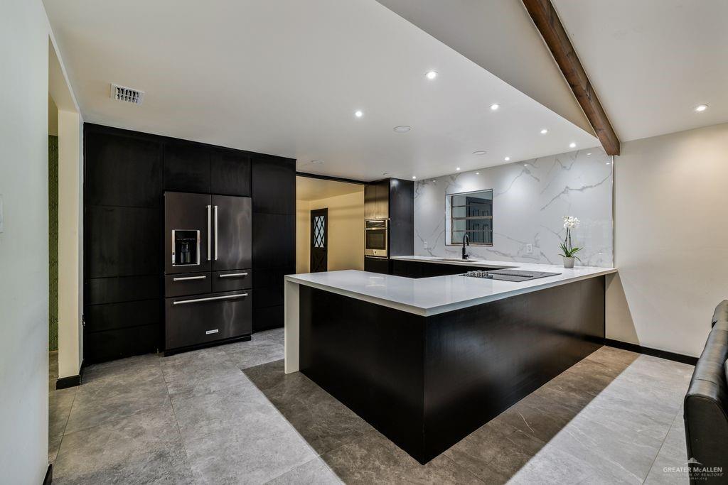111 South Cox Street Rio Grande City, TX 78582 - Photo 6 of 27 Kitchen with dark cabinets, recessed lighting, black appliances, beam ceiling, and a peninsula