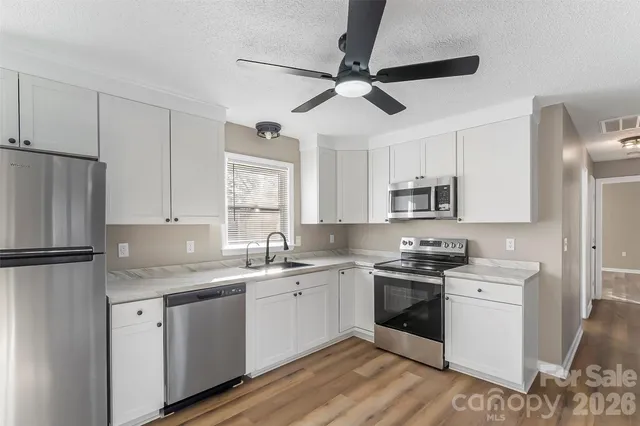 a kitchen with a sink stainless steel appliances white cabinets and wooden floor
