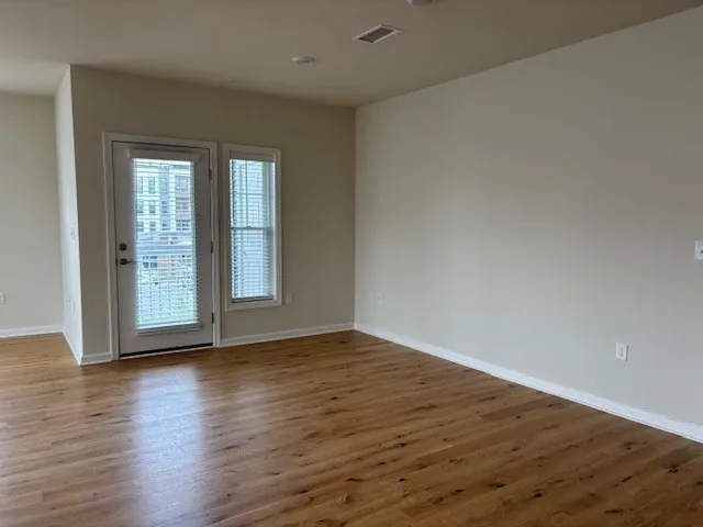 a view of an empty room with wooden floor and a window
