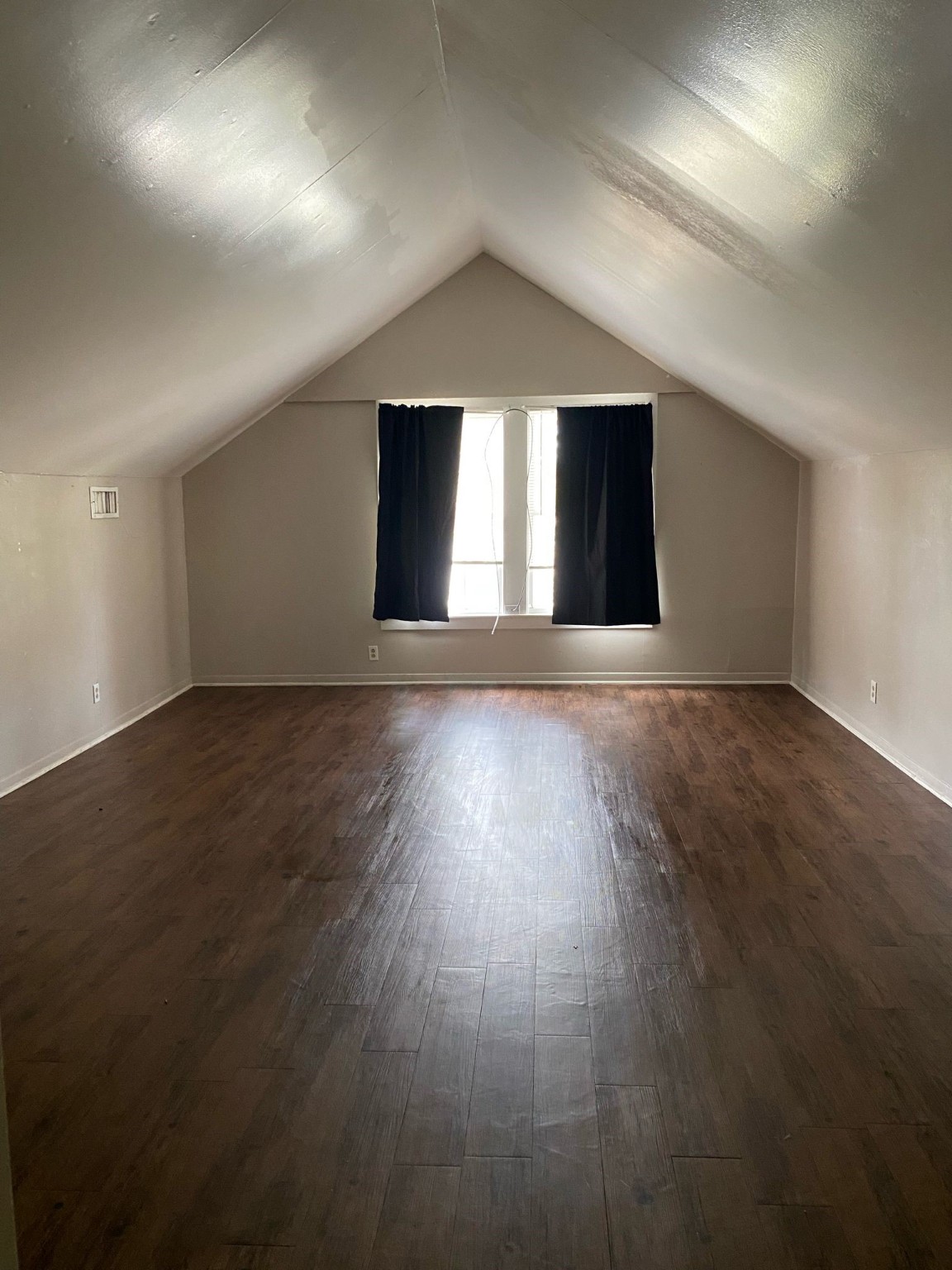 800 Travis Street, Unit ATTIC Columbus, TX 78934 - Photo 4 of 6 This room features a cozy attic space with a sloped ceiling, hardwood floors, and a large window with curtains. Ideal for a bedroom or home office.