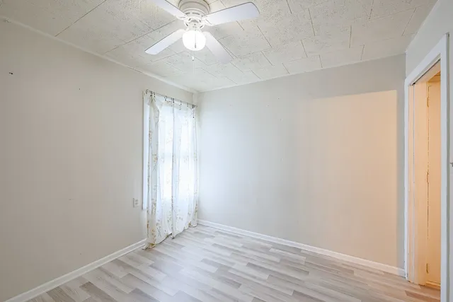 an empty room with wooden floor fan and windows