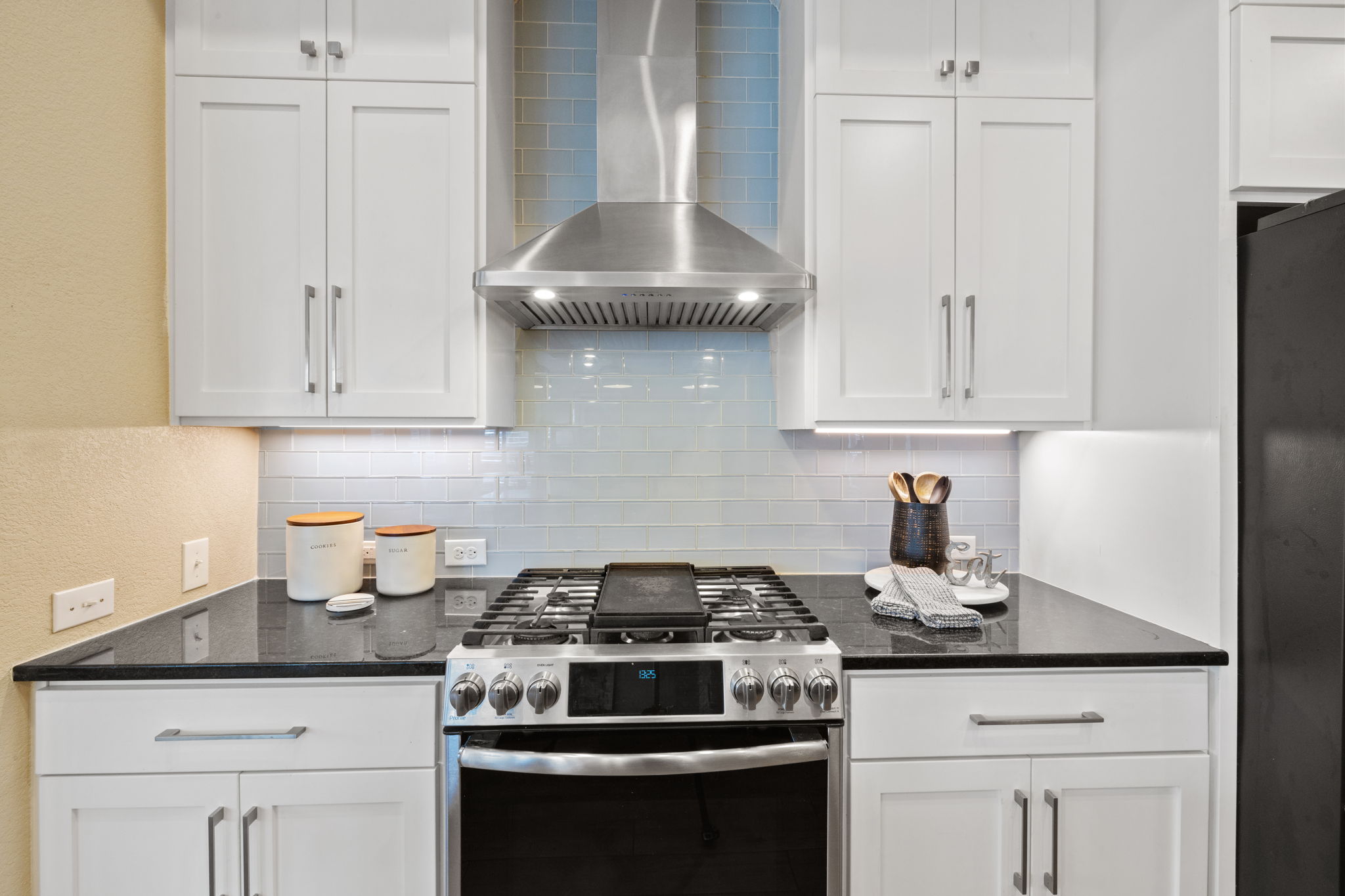 8112 Cobblestone Austin, TX 78735 - Photo 12 of 33 Kitchen with gas stove, wall chimney exhaust hood, black fridge, and decorative backsplash