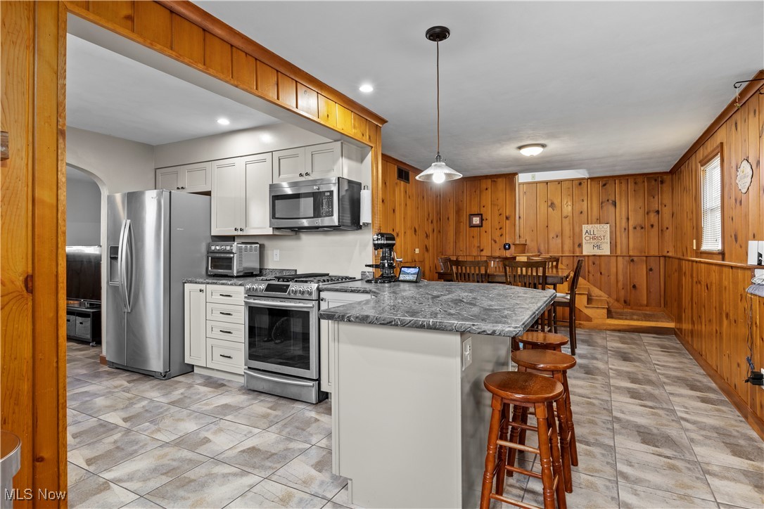 958 West River Road Vermilion, OH 44089 - Photo 10 of 40 Kitchen with appliances with stainless steel finishes, a kitchen breakfast bar, wooden walls, decorative light fixtures, and white cabinets
