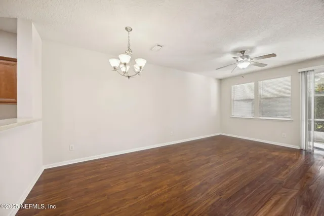 an empty room with wooden floor chandelier fan and windows