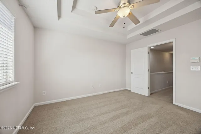 an empty room with chandelier fan and windows