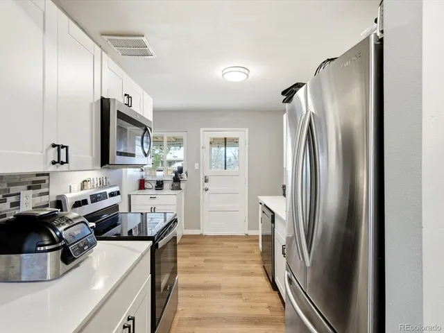 a kitchen with stainless steel appliances granite countertop a refrigerator a sink a stove and a refrigerator with wooden floor