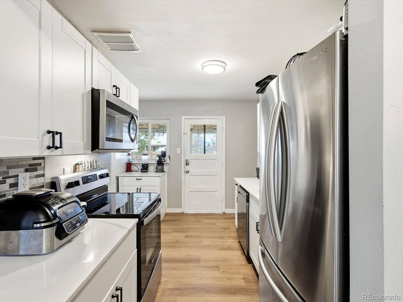 1883 South Perry Way Denver, CO 80219 - Photo 7 of 36 a kitchen with stainless steel appliances granite countertop a refrigerator a sink a stove and a refrigerator with wooden floor