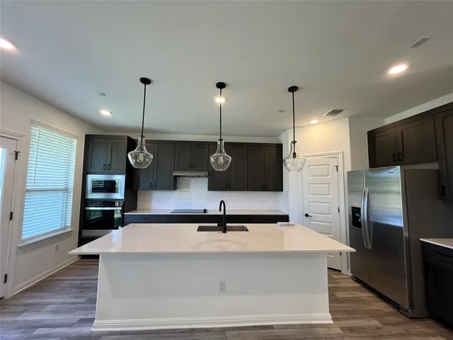 a large kitchen with stainless steel appliances a large counter top a sink a refrigerator and a stove