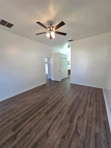 a view of an empty room with wooden floor and a ceiling fan
