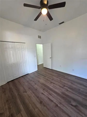 an empty room with wooden floor chandelier fan and windows