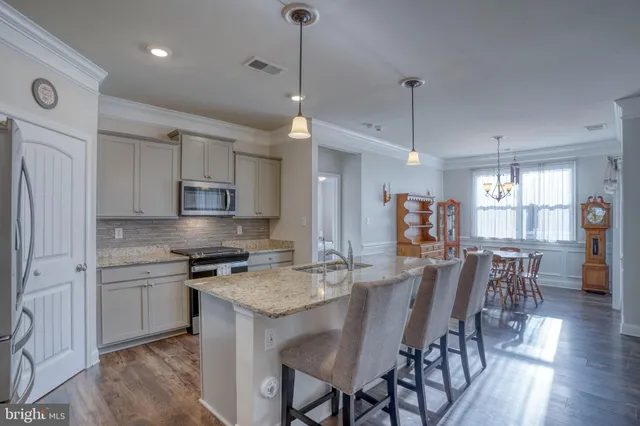 a kitchen with stainless steel appliances granite countertop a stove top oven a refrigerator a sink and a dining table with wooden floor