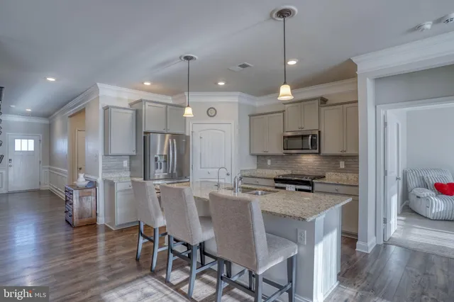 a kitchen with stainless steel appliances kitchen island granite countertop a stove a refrigerator a oven a sink with island and chairs with wooden floor