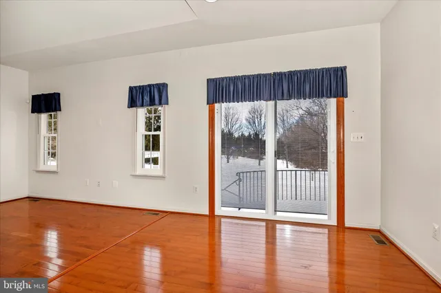 a view of an empty room with wooden floor and windows