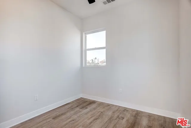 a view of an empty room with wooden floor and fan
