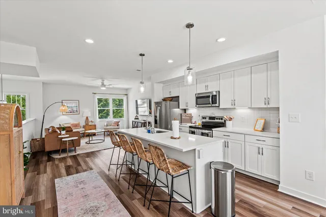 a view of a kitchen with kitchen island a stove a sink a refrigerator and a dining table with wooden floor