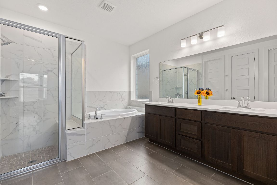 317 Independence Drive Kyle, TX 78640 - Photo 24 of 40 The en-suite bathroom, and it’s all about clean lines and crisp finishes. The walk-in shower with its glass enclosure and marble-look tile gives it that spa-like feel, and the dual sinks plus the dark wood vanity offer plenty of counter space, and the oversized mirror reflects even more light, keeping everything bright and airy.