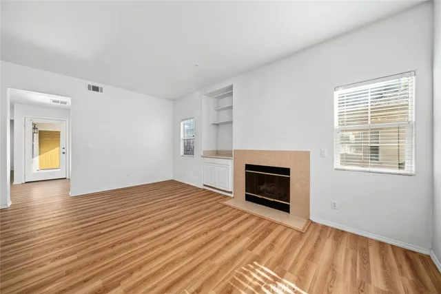 an empty room with wooden floor fireplace and windows