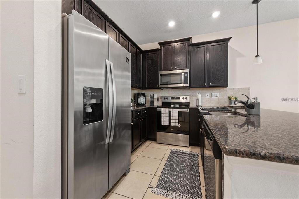 2449 Varenna Loop Kissimmee, FL 34741 - Photo 5 of 25 a kitchen with stainless steel appliances granite countertop a refrigerator a stove and a sink with wooden floor