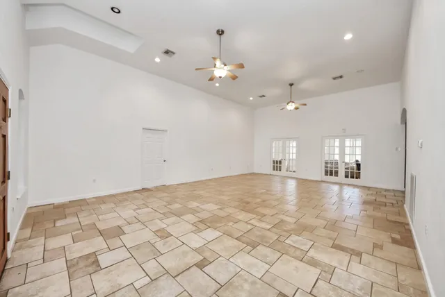 an empty room with kitchen view and a ceiling fan