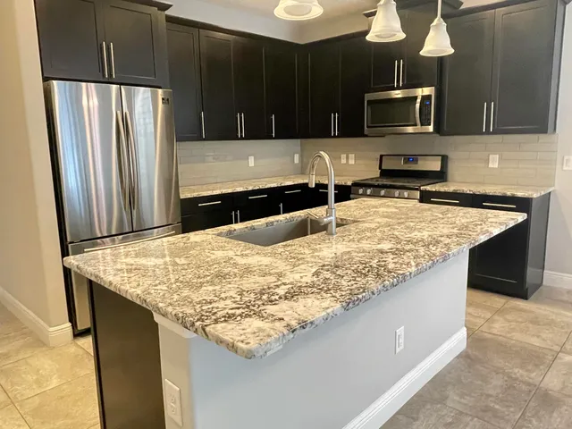 a kitchen with kitchen island granite countertop a sink refrigerator and microwave
