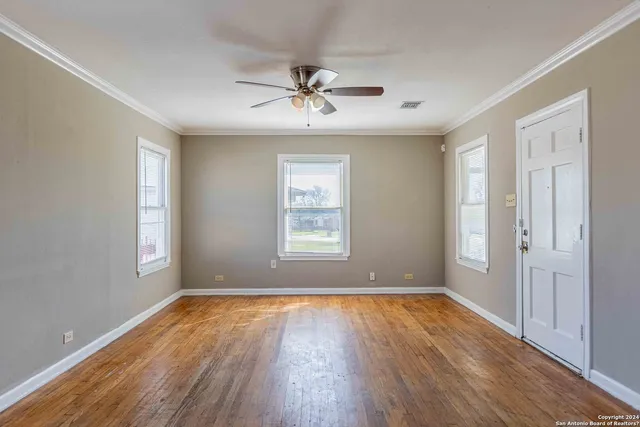 an empty room with wooden floor chandelier fan and windows