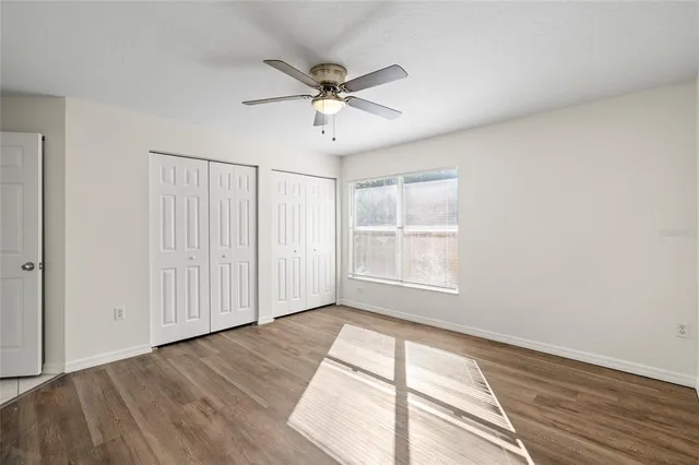 an empty room with wooden floor fan and windows
