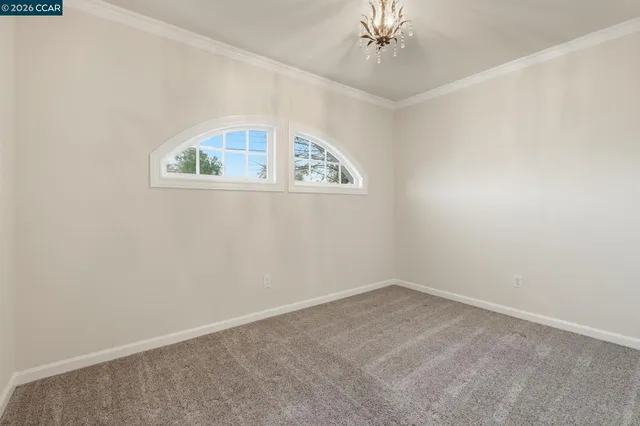 an empty room with a chandelier fan and a kitchen