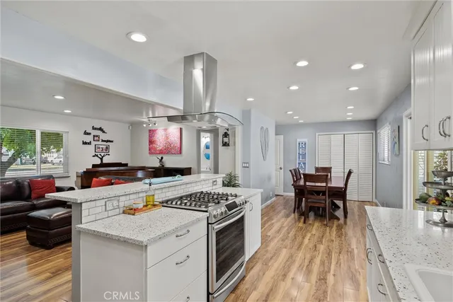 a kitchen with stainless steel appliances a stove a sink a oven a dining table and chairs with wooden floor