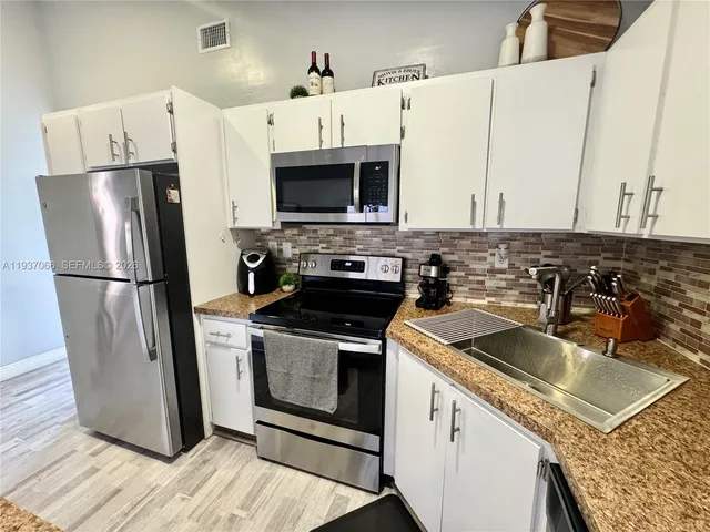 a kitchen with stainless steel appliances granite countertop a refrigerator a stove a sink and white cabinets