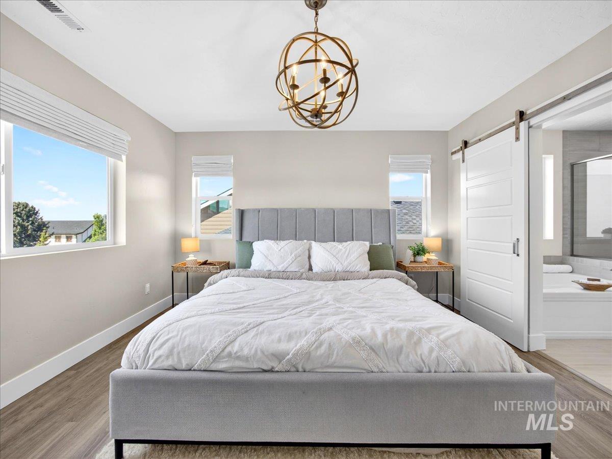 1811 Rome Avenue Emmett, ID 83617 - Photo 28 of 50 Bedroom featuring wood-finish flooring, a contemporary chandelier, two windows, and a sliding barn door leading to an adjacent bathroom with a built-in tub