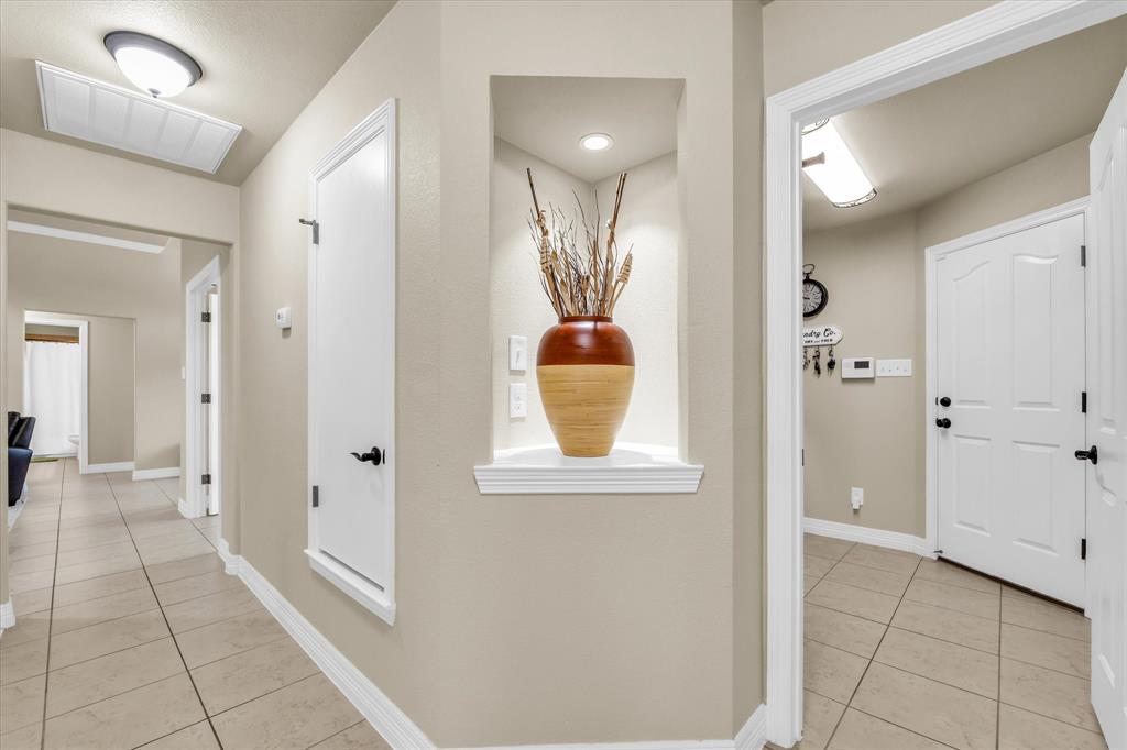 910 Springdale Lane Lorena, TX 76655 - Photo 19 of 39 Neutral-toned hallway featuring tile flooring, white baseboards, and a recessed wall niche with accent lighting
