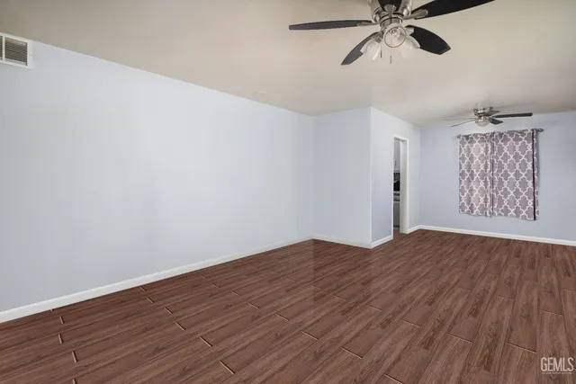 an empty room with wooden floor fan and windows