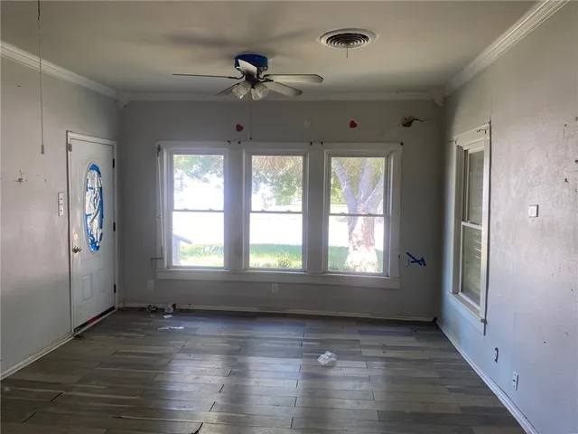 an empty room with wooden floor fan and windows