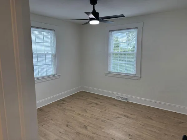 an empty room with wooden floor ceiling fan and windows