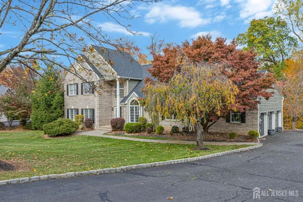 a view of a white house next to a yard with big trees and plants