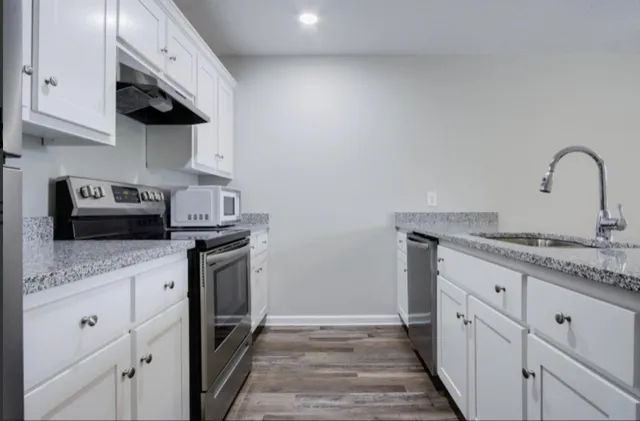 a kitchen with granite countertop a sink stainless steel appliances and white cabinets