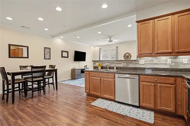 a kitchen with stainless steel appliances granite countertop a stove top oven a sink dishwasher a dining table and chairs with wooden floor