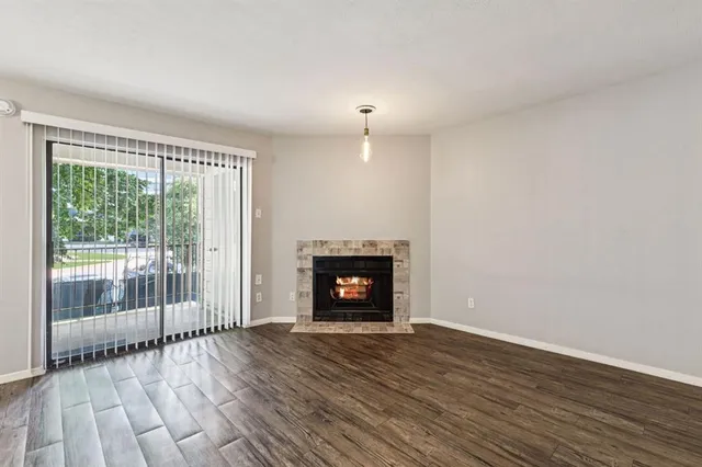 a view of an empty room with wooden floor fireplace and a window