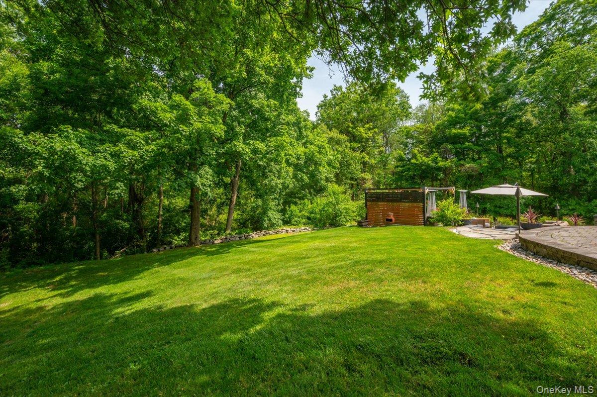 13 Jacks Pond Road Newburgh, NY 12550 - Photo 36 of 44 Expansive lawn area bordered by mature trees, featuring a stone retaining wall and a patterned paver patio.