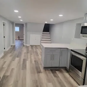 a view of an empty room with wooden floor and a kitchen