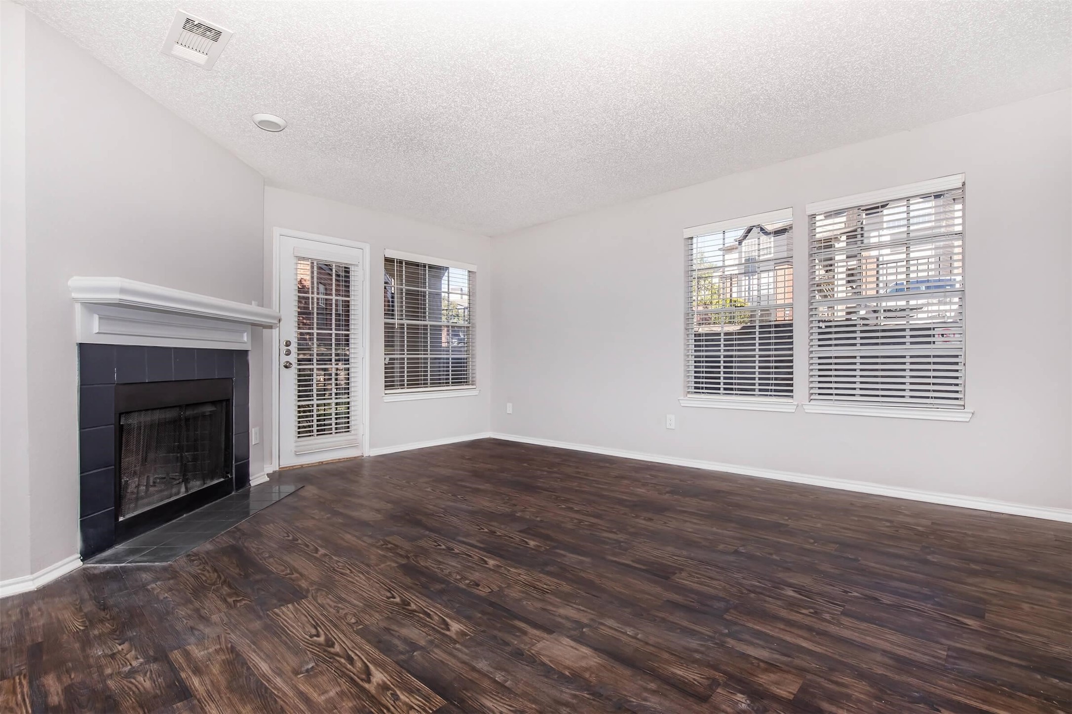 a view of an empty room with wooden floor fireplace and a window