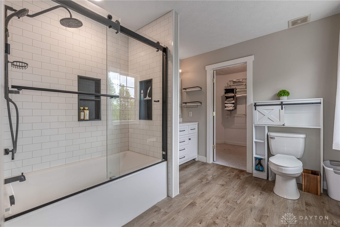 9586 Ferry Road Waynesville, OH 45068 - Photo 15 of 40 This primary bathroom boasts a sophisticated tiled shower with a glass enclosure and elegant wood-style flooring.