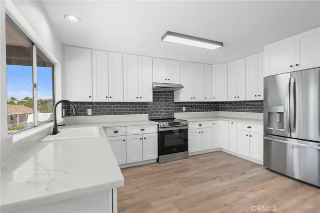a kitchen with granite countertop a refrigerator sink stove and white cabinets